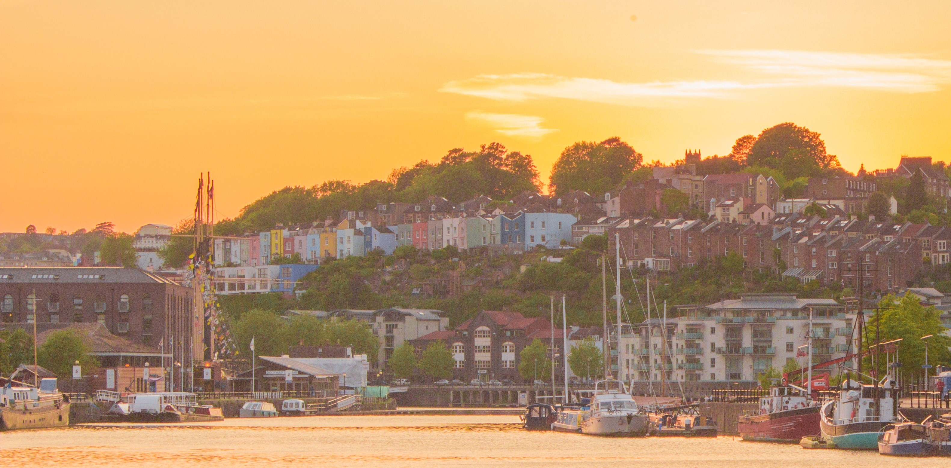 Bright sunset at Bristol harbourside reflects on water, a backdrop to boats and colourful houses